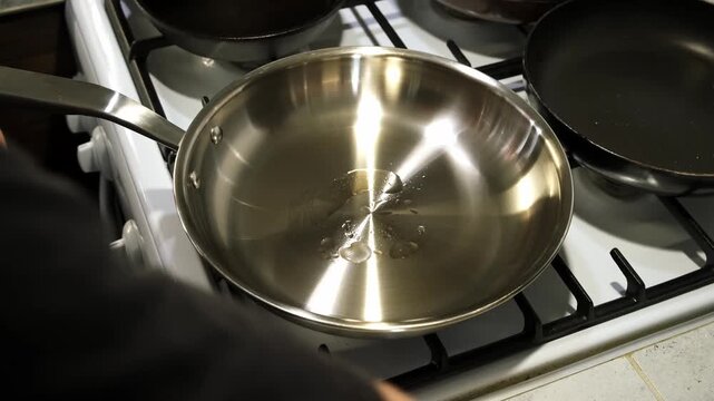 person cooking pours oil into stainless frying pan on stove in kitchen with multiple pots and pans top-down view. High quality 4k footage.