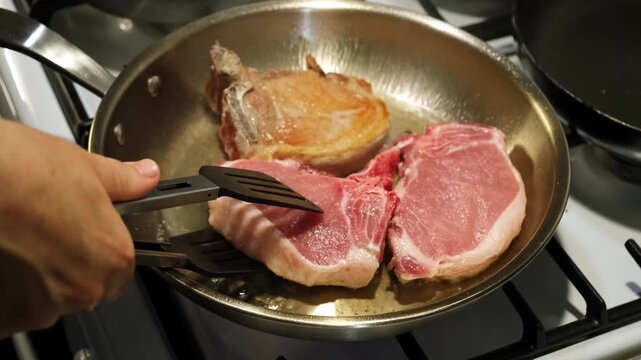 Cooking pork chops flipping pork chops in a pan, in kitchen stove with stainless steel pan, with pork chops, pan, stove, with metallic pan, wooden spatula texture, with silver, pink accents.