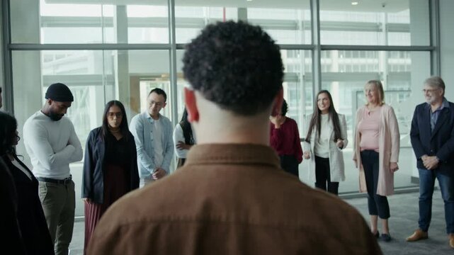Diverse business professionals gather in an open space, looking at the speaker. This represents teamwork, collaboration, and learning, fostering unity and engagement for a discussion.