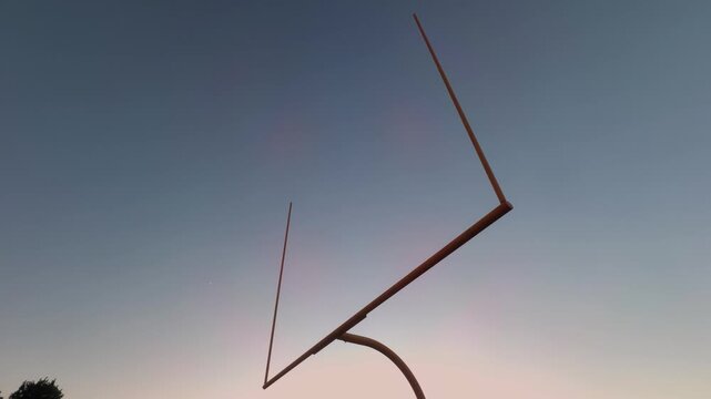 Wide-angle slow downward pan of an American football goal post silhouetted against a colorful sunset sky.