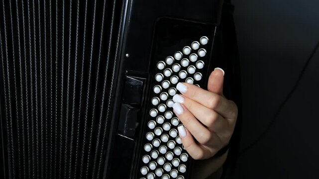 Close-up of hand playing bass buttons of black accordion, fingers press white circular buttons on musical instrument, detail of performance, musician skill for music generation.