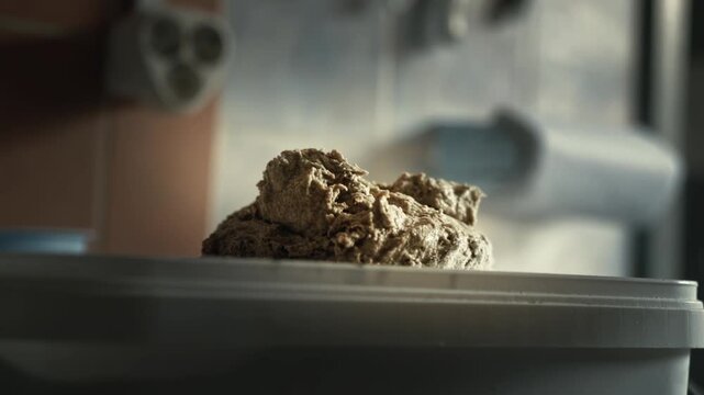 Close-up ready-made dough piece is in container. Kitchen of private bakery, raw baking ingredient, rustic texture. Food preparation process for bread or pastry making. Small business bread production