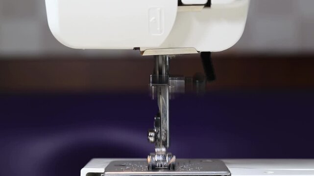 Close-up view of needle and presser foot of white modern sewing machine in operation, stitching fabric, process of creating garments, fashion industry equipment