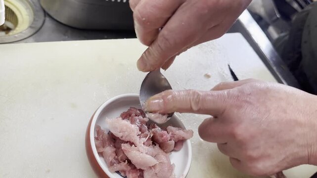 Chef scraping tuna meat from the tail bone onto a plate of minced tuna