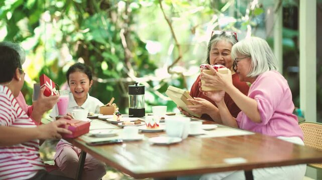 Group of senior friends happily exchanges gifts while celebrating together. Friendship, kindness, appreciation and active aging create meaningful moments and positive retirement lifestyle.