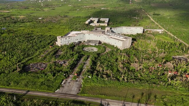 Aerial view of the abandoned Tinian Dynasty Hotel surrounded by overgrown tropical vegetation and palm trees in Taga Beach, Tinian, Northern Mariana Islands.