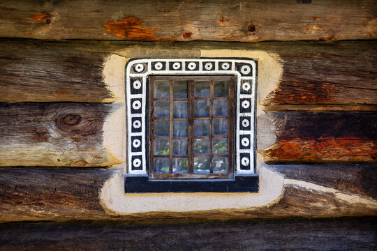 Vintage decorated window on old wooden log cabin wall. Rustic window with ethnic painted ornaments on authentic wooden log house facade. Ideal for travel guides, heritage tourism promos
