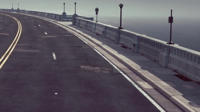 A road runs beside the ocean with light posts on the side. Water can be seen in the distance. No cars are on the road. The weather looks cloudy and quiet.