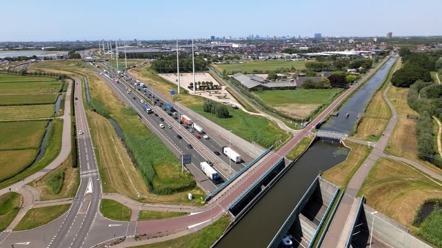 Aerial view of the A4 motorway with traffic flowing alongside a canal and green agricultural fields in Den Hoorn, South Holland, Netherlands.