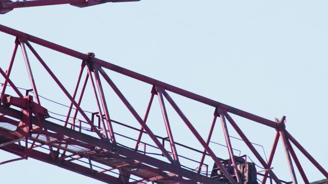 Red metal truss structure of large crane boom against clear light blue sky heavy construction equipment detail industrial machinery engineering design apparatus robust framework