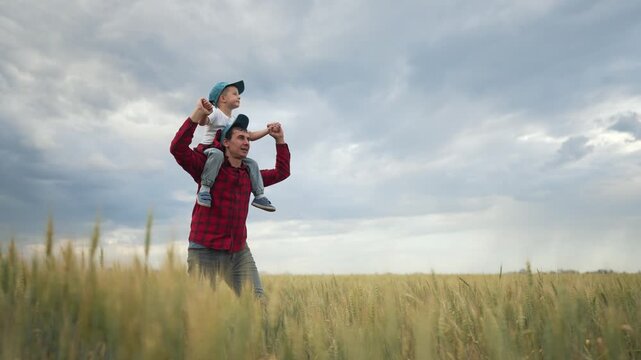 Father carries son on shoulders in field. Family enjoys playful moment. Father son bonding from back view. play outdoors. Family values in nature. family time in field. Playful family moment outdoors.