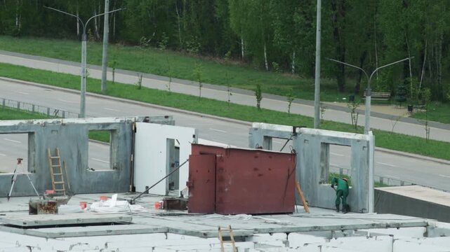 Worker Prepares Concrete Panel On Rooftop. Construction Site Overlooks Passing Traffic.