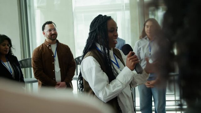 Diverse professionals at a conference. A woman speaks excitedly into a microphone, sharing ideas, creating a positive, collaborative atmosphere among smiling colleagues.