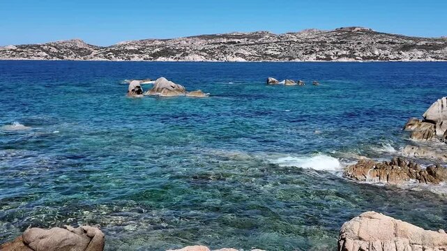 Rocky coastline still scene with no action, in beachside landscape, with rocks, clear blue water, mountains in the background, with rocky formations, water texture.