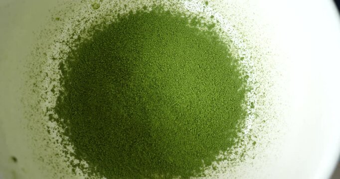 Matcha Powder Macro Shot: A finely ground mound of vibrant green matcha powder, sprinkled artfully on a smooth white surface, showcasing the texture and color of this popular tea ingredient.