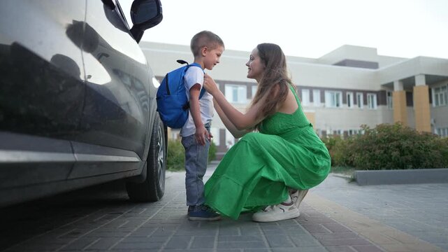 Mother with child and backpack. Family moment by car. Mother supports son with backpack. Happy child at school drop off. Family first school day. Excited child loving mother. Car family backpack scene