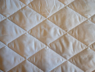 Fototapeta premium Beige quilted fabric texture with a geometric diamond pattern. Ideal backdrop for bedding catalogs, home textile website banners, or mattress manufacturing blogs.