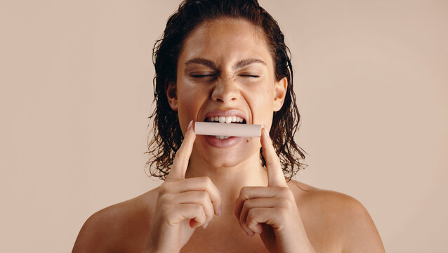 Woman biting unbranded lip balm in minimalist studio shoot