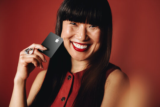 Smiling woman uses a black credit card in a studio portrait for consumer finance