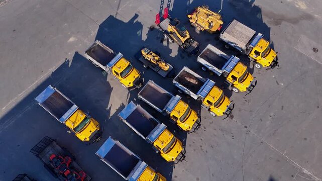 Aerial view of a fleet of yellow construction dump trucks parked in a lot