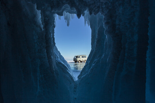 View of a UAZ van parked on the frozen surface of Lake Baikal, framed by jagged blue ice formations in Khuzhir, Irkutsk Oblast, Russia.