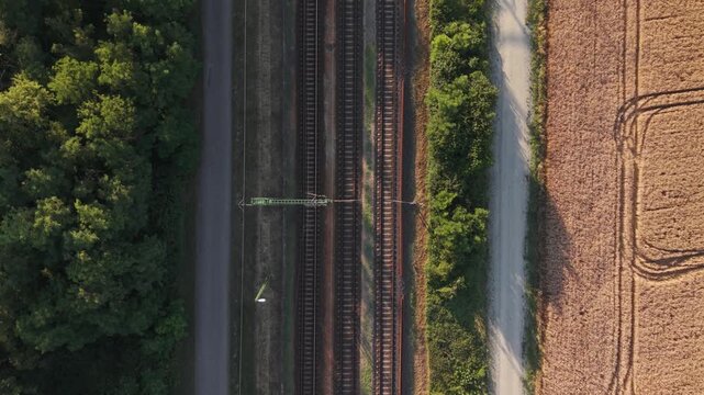 A top-down aerial view of parallel railway tracks running between a dense green forest and golden agricultural fields.