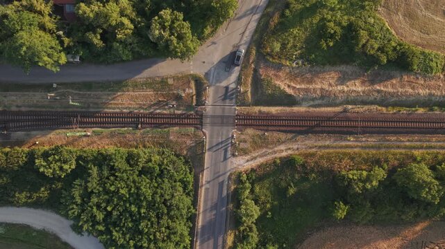 A top-down drone view of a rural railway level crossing where a local road intersects parallel railroad tracks.