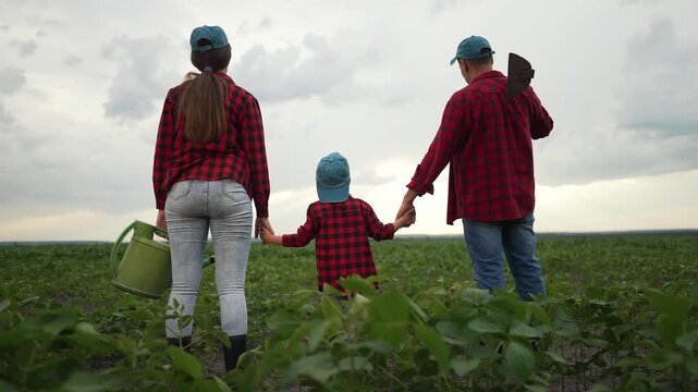 Farmers with hoe sprinkler in field. Family working on crop together. Rural farming lifestyle. Parents child holding hands. Farmers united field. Hoe and sprinkler in farming. Crop cultivation scene.