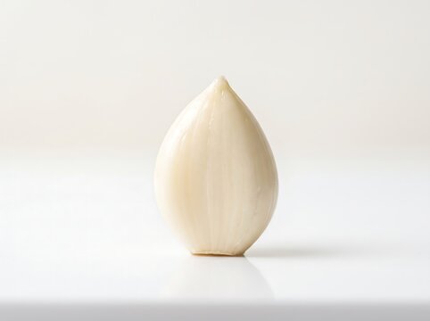 A single perfect peeled garlic clove standing on a white surface