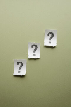 Three torn paper question marks on olive green background representing business choice and uncertainty