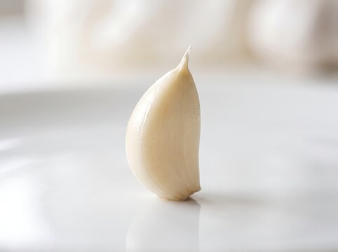 A single perfect peeled garlic clove standing on a white surface