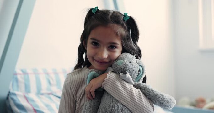 Face, hug and little girl with teddy bear in bedroom of home for comfort, love or security. Child development, morning and smile with cute kid embracing stuffed animal on bed in apartment for care
