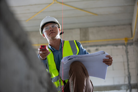 Construction professional utilizing a laser level to accurately measure dimensions at a job site while holding blueprints
