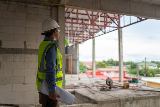 Construction worker monitoring the progress of an industrial site while holding blueprints at a building project
