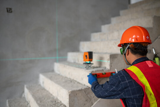 Construction professional using a laser level to ensure accurate measurements on a staircase project at a job site
