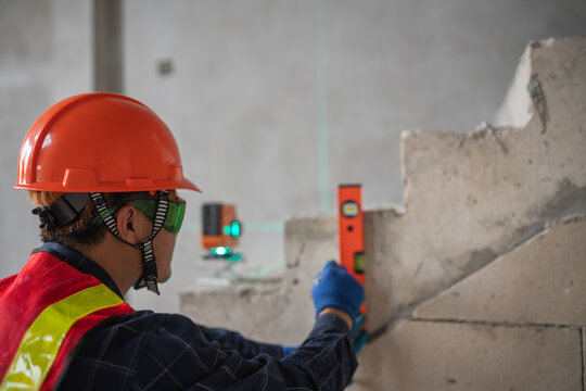 Construction professional utilizing a leveling tool for precise measurements at a building site while wearing protective equipment
