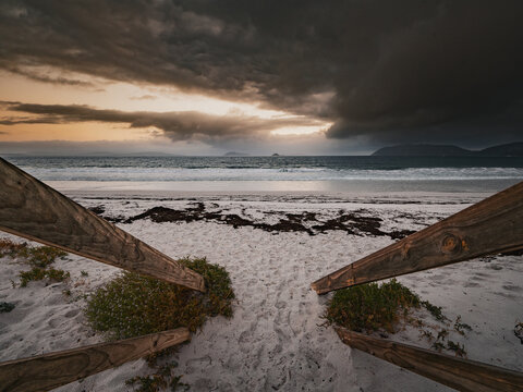 View of Goode Beach with a wooden walkway leading to the white sand shore under dramatic storm clouds at sunset in Albany, Western Australia, Australia.