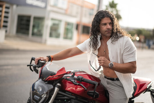 Long Haired Man Leaning on Red Naked Motorcycle at Golden Hour