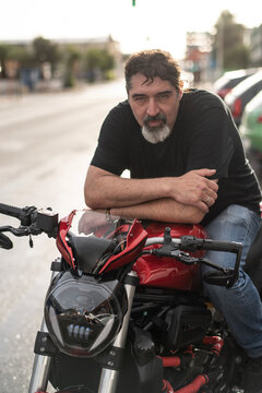 Bearded Man Leaning on Red Naked Motorcycle at Golden Hour