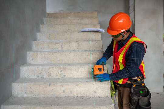 Construction professional utilizing a laser level for accurate measurements on a staircase in an industrial environment