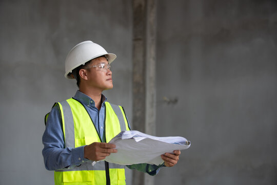 Focused construction worker reviewing blueprints on job site with safety gear and professional attire