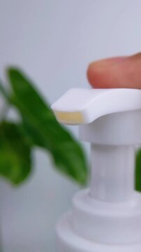 Macro shot of a skincare pump bottle releasing a clear serum drop, set against a minimalist white background with soft botanical accents.