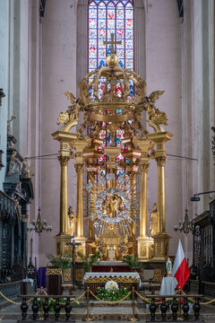 Close-up view of an elaborate, highly ornate golden altar inside a historic church, featuring intricate carvings, statues, and a central radiating design, set against a stained glass window.