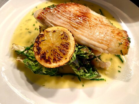 Pan-seared skate wing served with a rich creamy herb sauce, charred lemon, and seasonal green vegetables. Elegant seafood main course beautifully presented on a white plate, ideal for fine dining, res