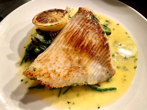 Pan-seared skate wing served with a rich creamy herb sauce, charred lemon, and seasonal green vegetables. Elegant seafood main course beautifully presented on a white plate, ideal for fine dining, res