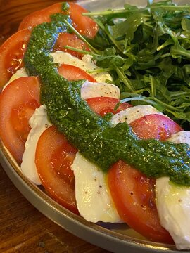 Fresh Caprese salad made with sliced mozzarella, ripe tomatoes, basil pesto, and rocket leaves. Colourful Italian-inspired dish served in a bowl, ideal for healthy eating, vegetarian cuisine, 