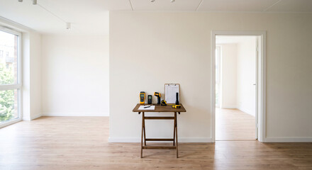 Fototapeta premium Wide empty living room with wood flooring, open doorway, and inspection instruments displayed on a small table against a white wall