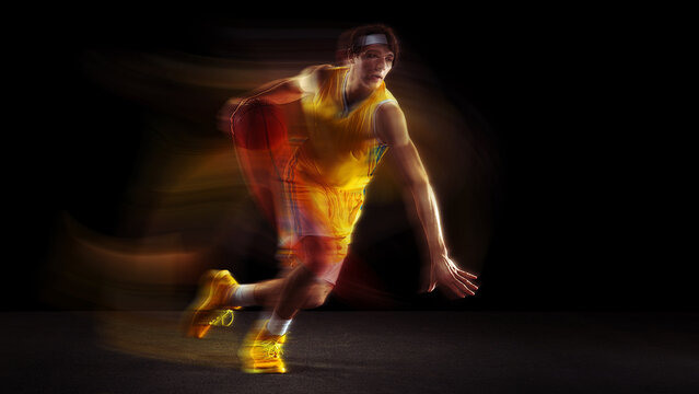 Basketball player dribbling with colorful motion blur in dramatic studio lighting. Concept of sports media, event posters, mobile apps, fan engagement, digital marketing.