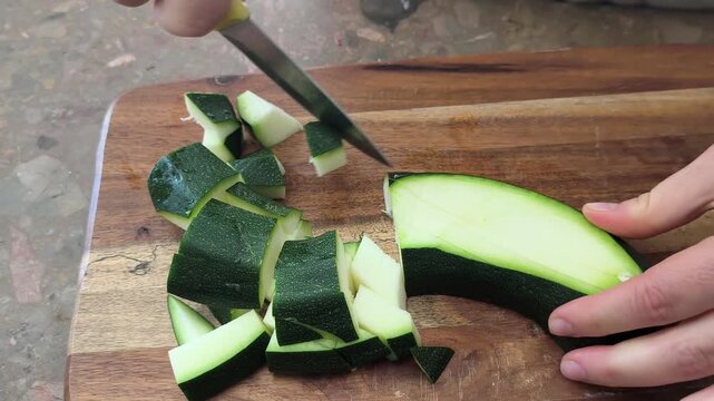 Young green zucchini are cut with a knife on a wooden board on the table