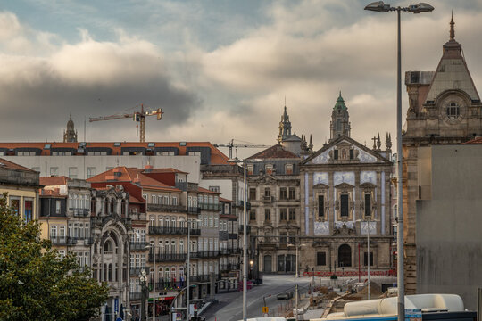Vista de la arquitectura tradicional portuguesa en Oporto, destacando una iglesia con azulejos t&iacute;picos, edificios antiguos con balcones y calles en obras bajo un cielo nublado.